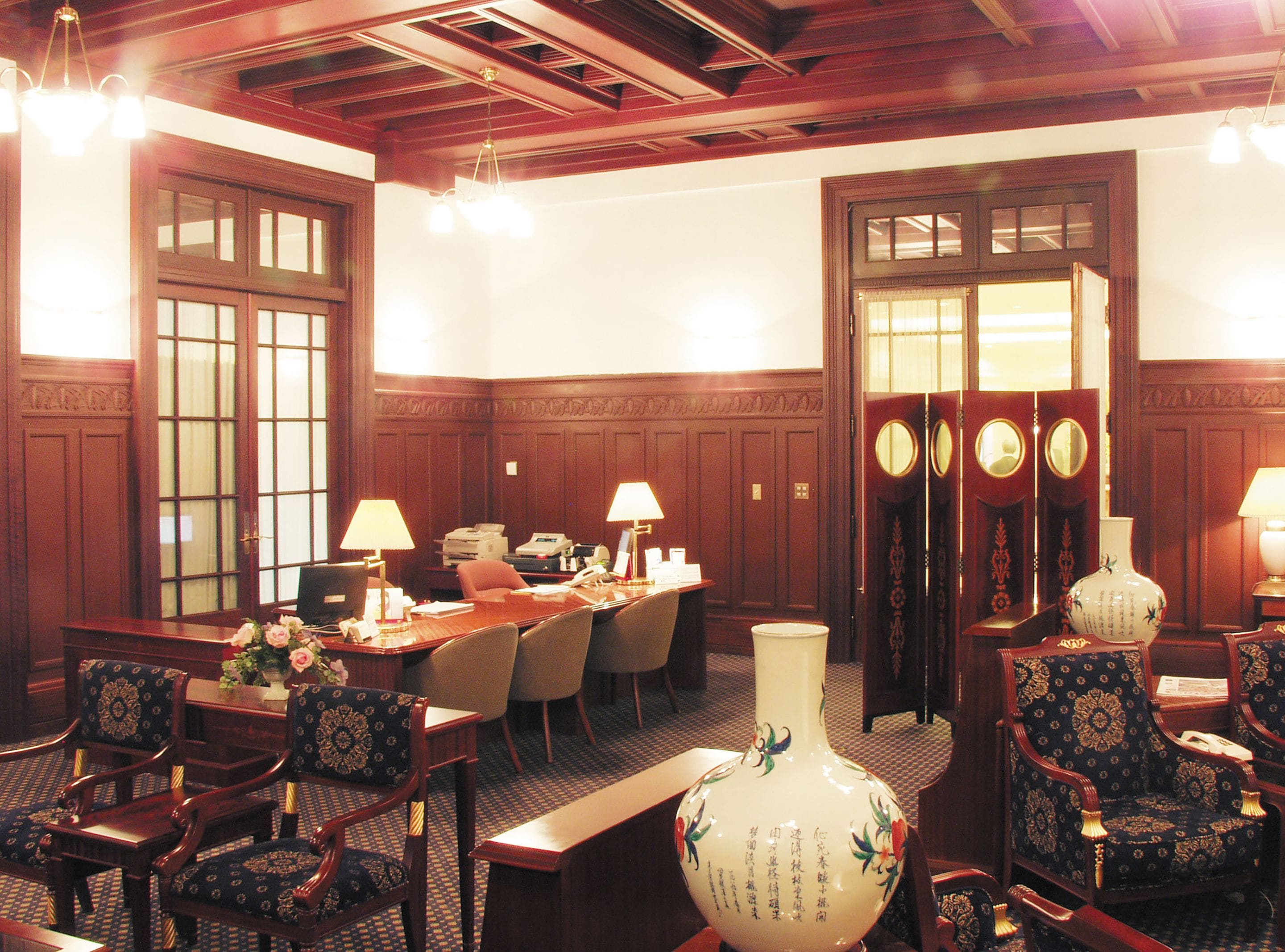 A formal dining room with wooden paneling, a large vase, and a conference table with chairs.