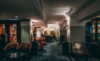 A hotel lobby with a patterned floor, leather chairs, a bar area, and a display of bottles.