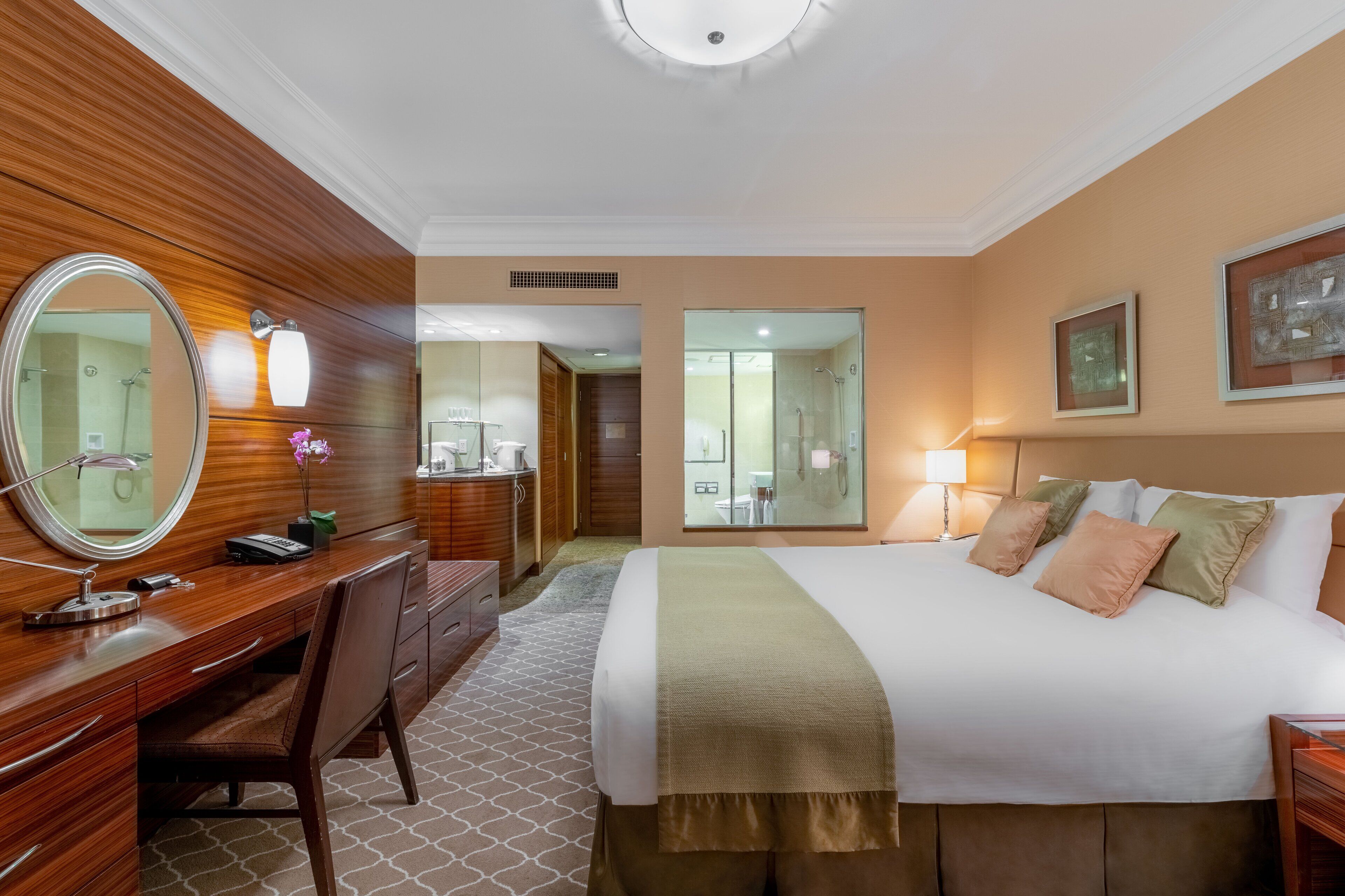 Ein Hotelzimmer mit einem Holztisch, einem großen Bett, einem Spiegel und einem durch eine geöffnete Tür einsehbaren Badezimmer.
