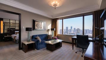 A hotel room with a city view, a sofa, a desk, and a television.