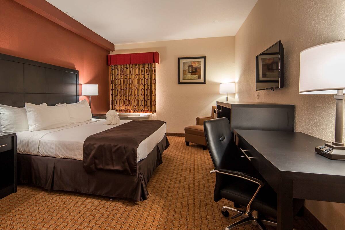 A hotel room with a bed, bedside tables, a desk, a chair, and a TV.