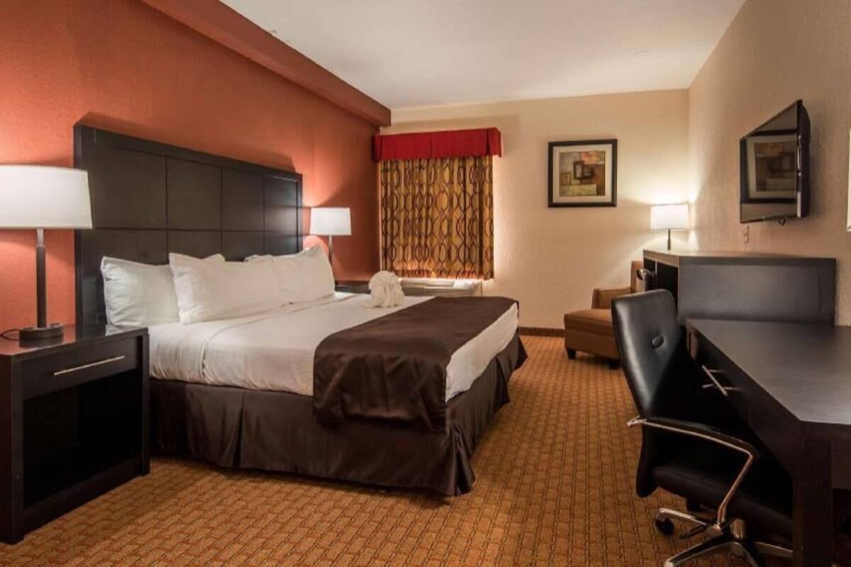 A hotel room with a bed, desk, chair, and lamps.