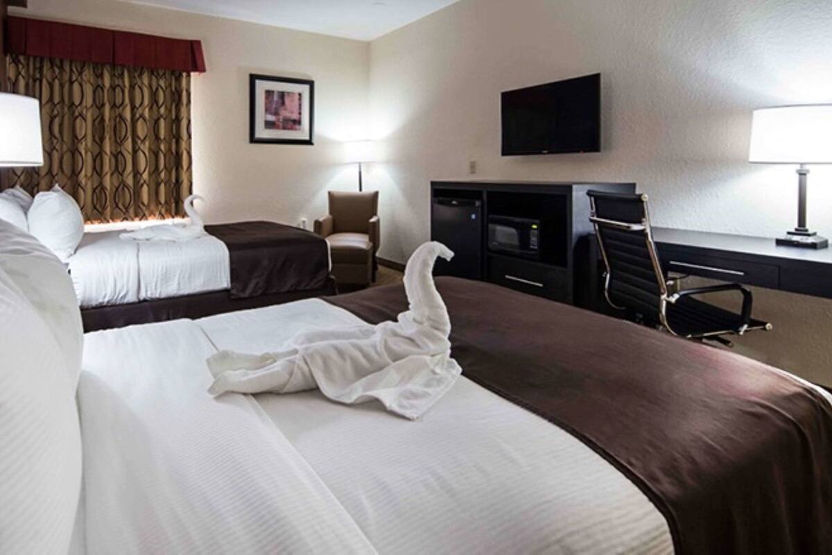 A hotel room with two beds, a desk, a chair, a television, and a fireplace.