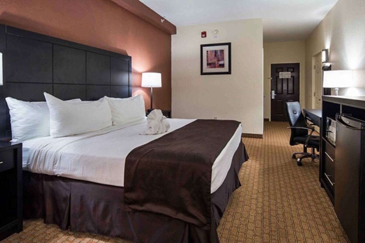 A hotel room with a large bed, a desk with a computer, a TV, and a refrigerator.