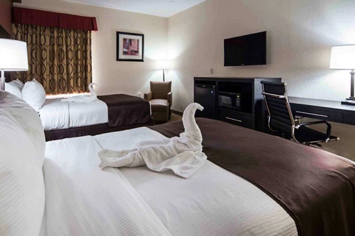 A hotel room with two beds, a desk, a chair, a television, and a fireplace.