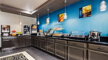 Una barra de desayuno moderna con pared azul, máquinas de café y diversas opciones de comida.