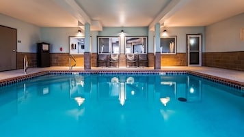 Una piscina con borde de azulejos, un área de estar con sillas y una pared con un cartel.
