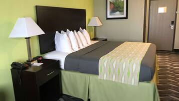 A hotel room with a bed, bedside lamps, a nightstand with a phone, a framed picture on the wall, and a door.