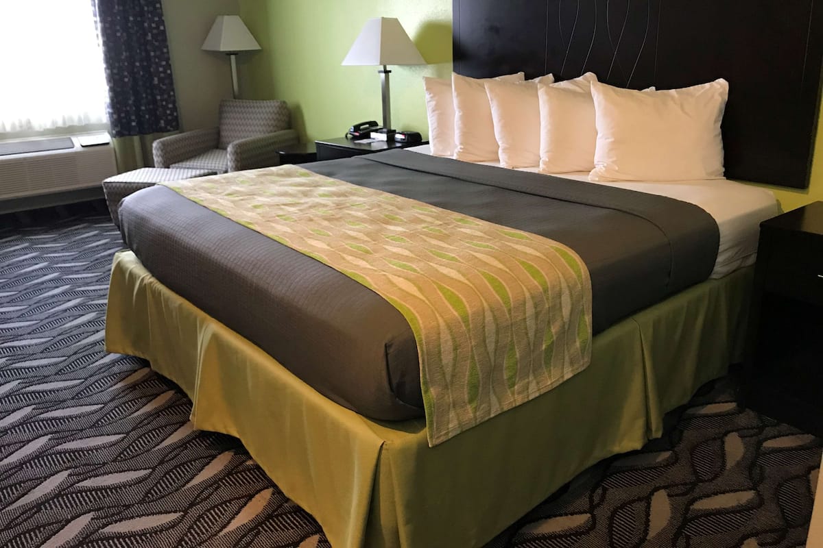 A hotel room with a large bed, a bedside table with a lamp, a chair, and a window with curtains.