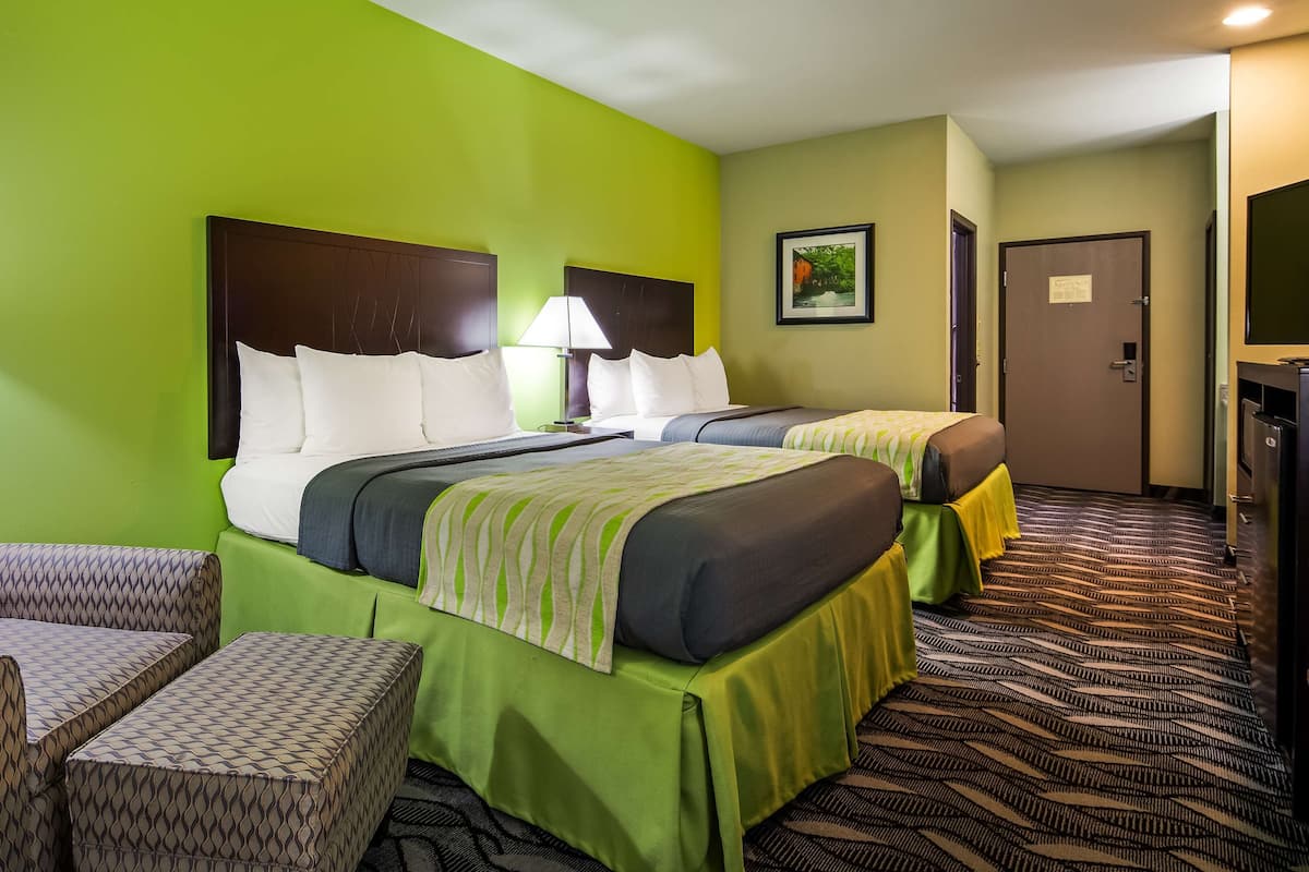A hotel room with two beds, a green wall, a patterned armchair, and a desk with a lamp.