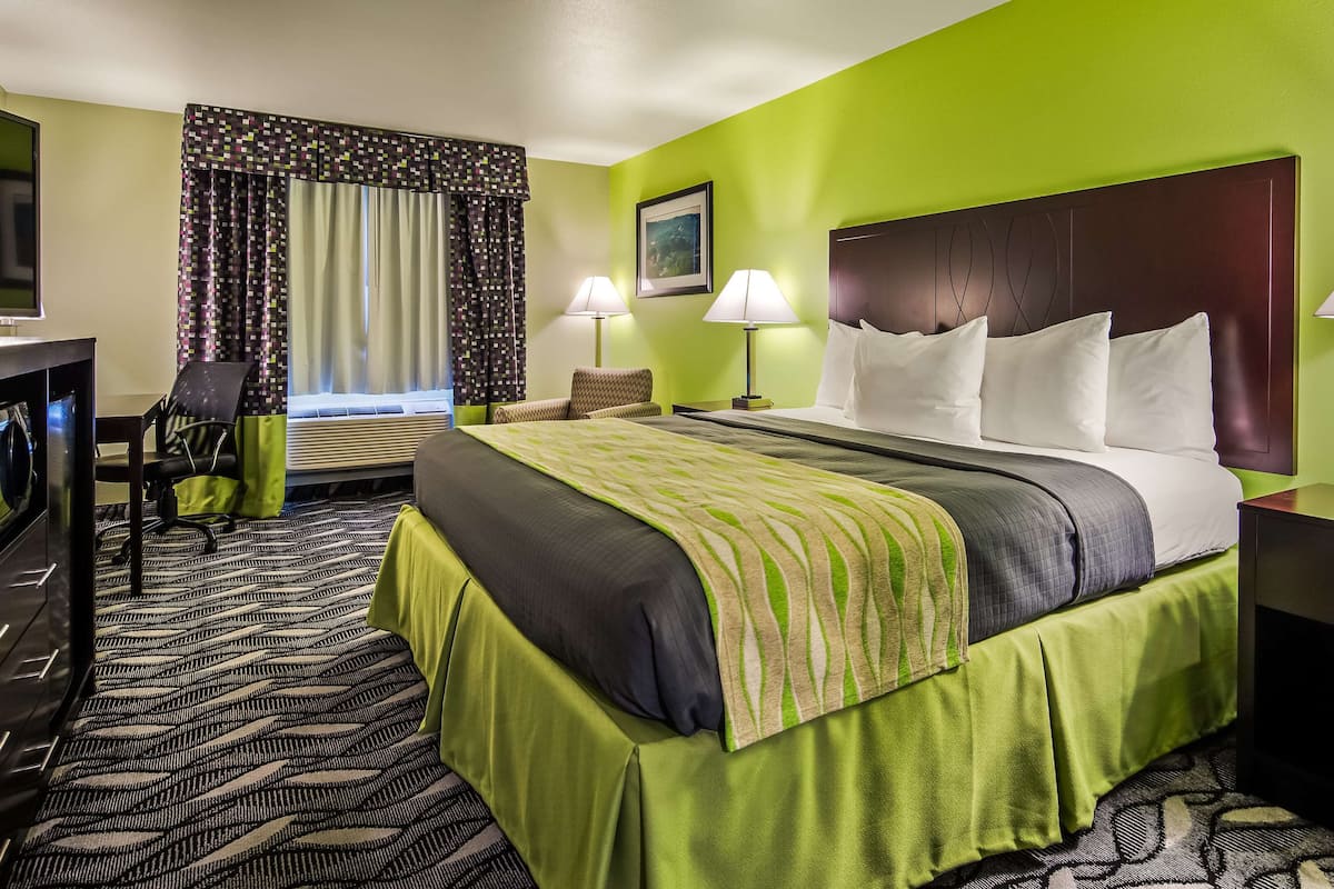 A hotel room with a bed, two bedside lamps, a desk with a computer, a chair, and a window with curtains.