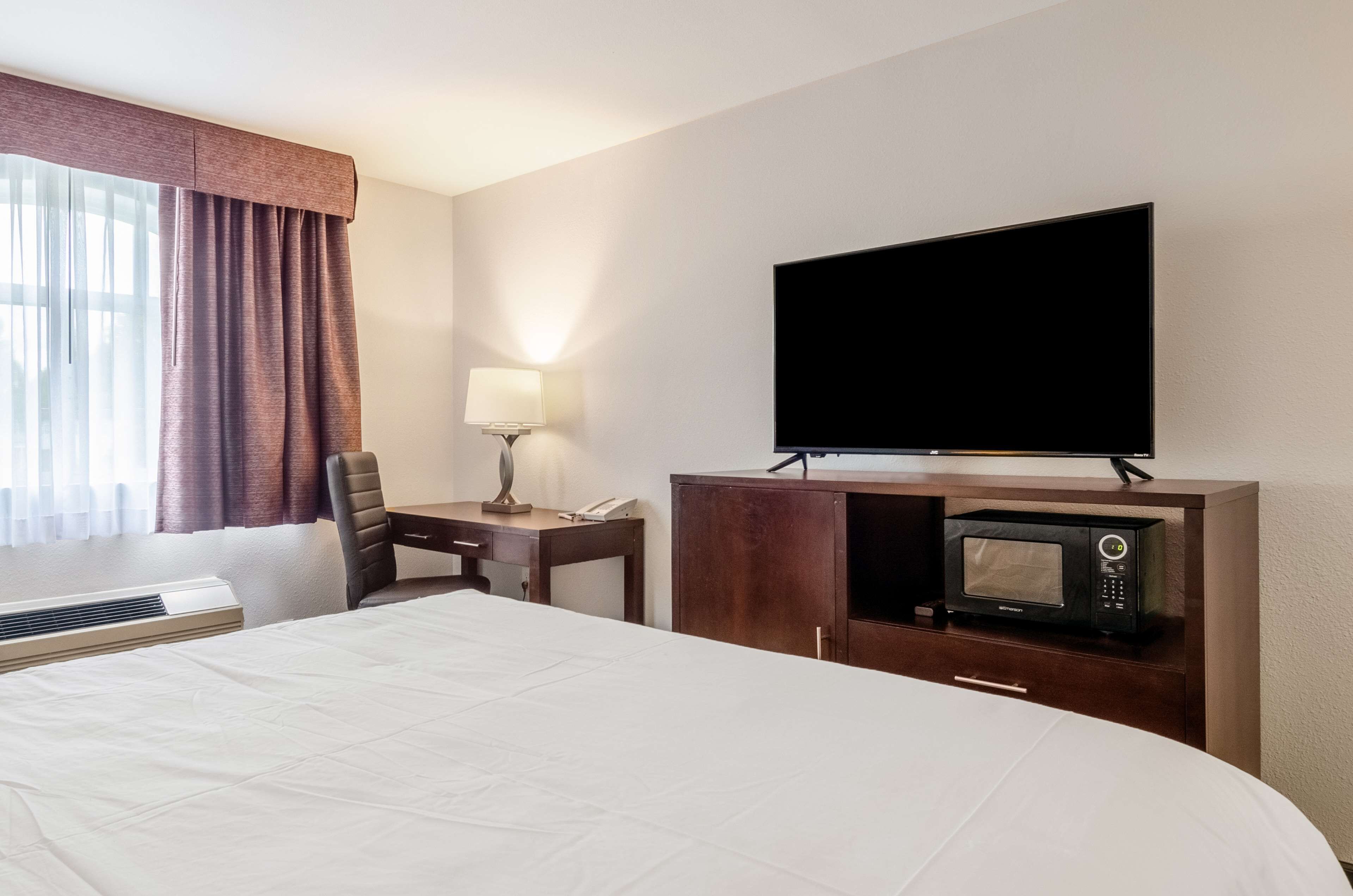 A hotel room with a bed, a desk with a lamp, a television, and a microwave.