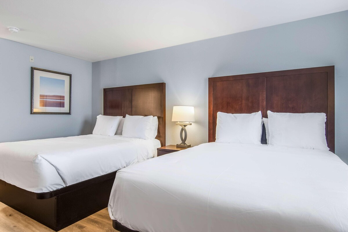 A hotel room with two beds, a nightstand with a lamp, and a framed picture on the wall.