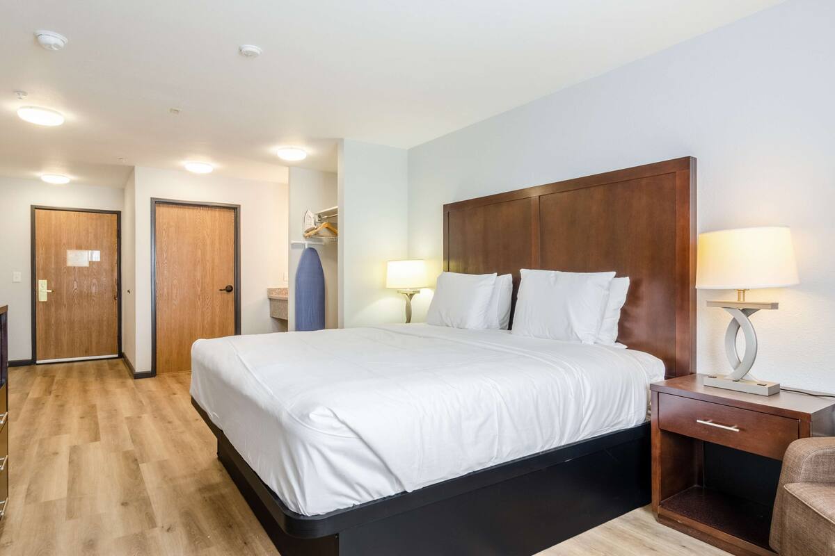 A hotel room with a large bed, two bedside tables with lamps, a wooden wardrobe, and a small seating area.