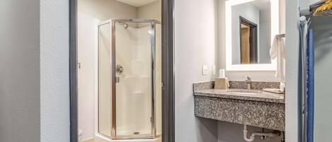 A modern bathroom with a glass shower enclosure, a granite countertop sink, and a mirror with integrated lighting.
