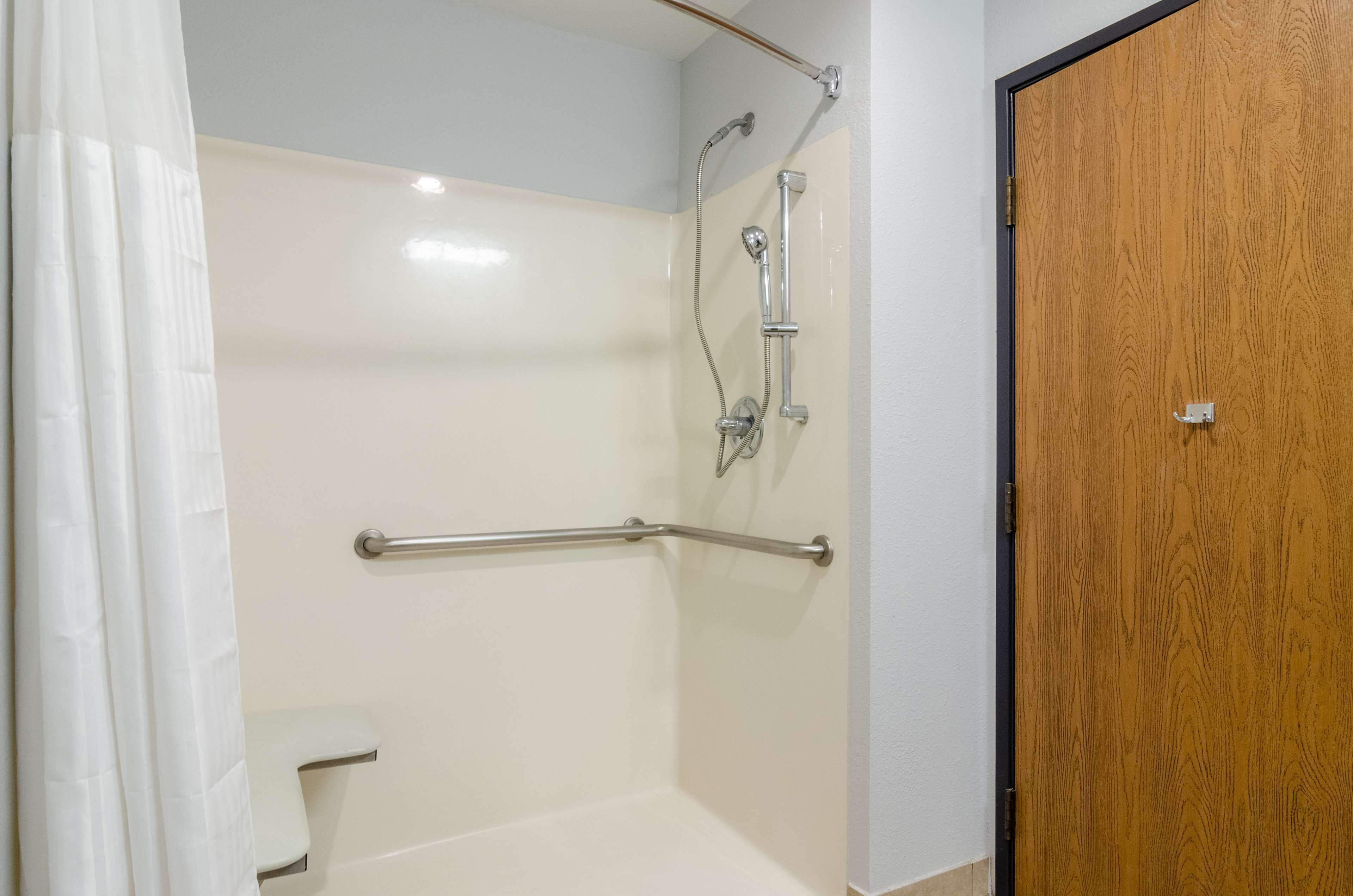 A shower area with a grab bar, a showerhead, and a wooden door.