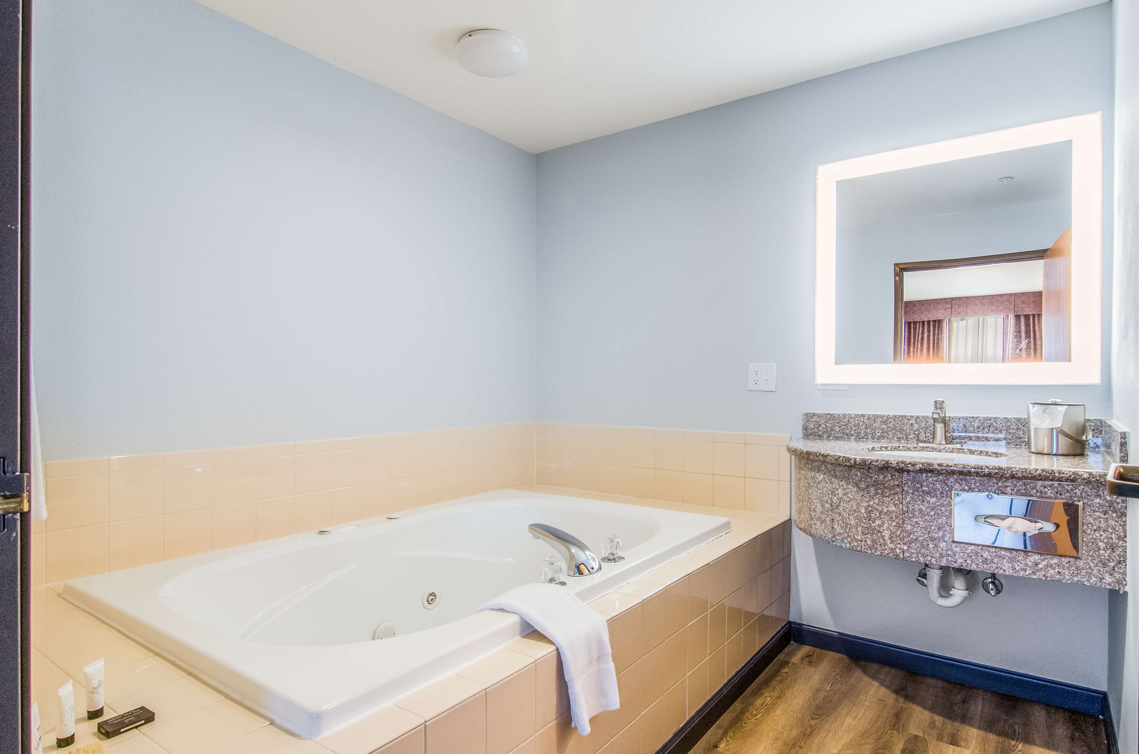 A modern bathroom with a large bathtub, a vanity with a mirror, and a small sink.