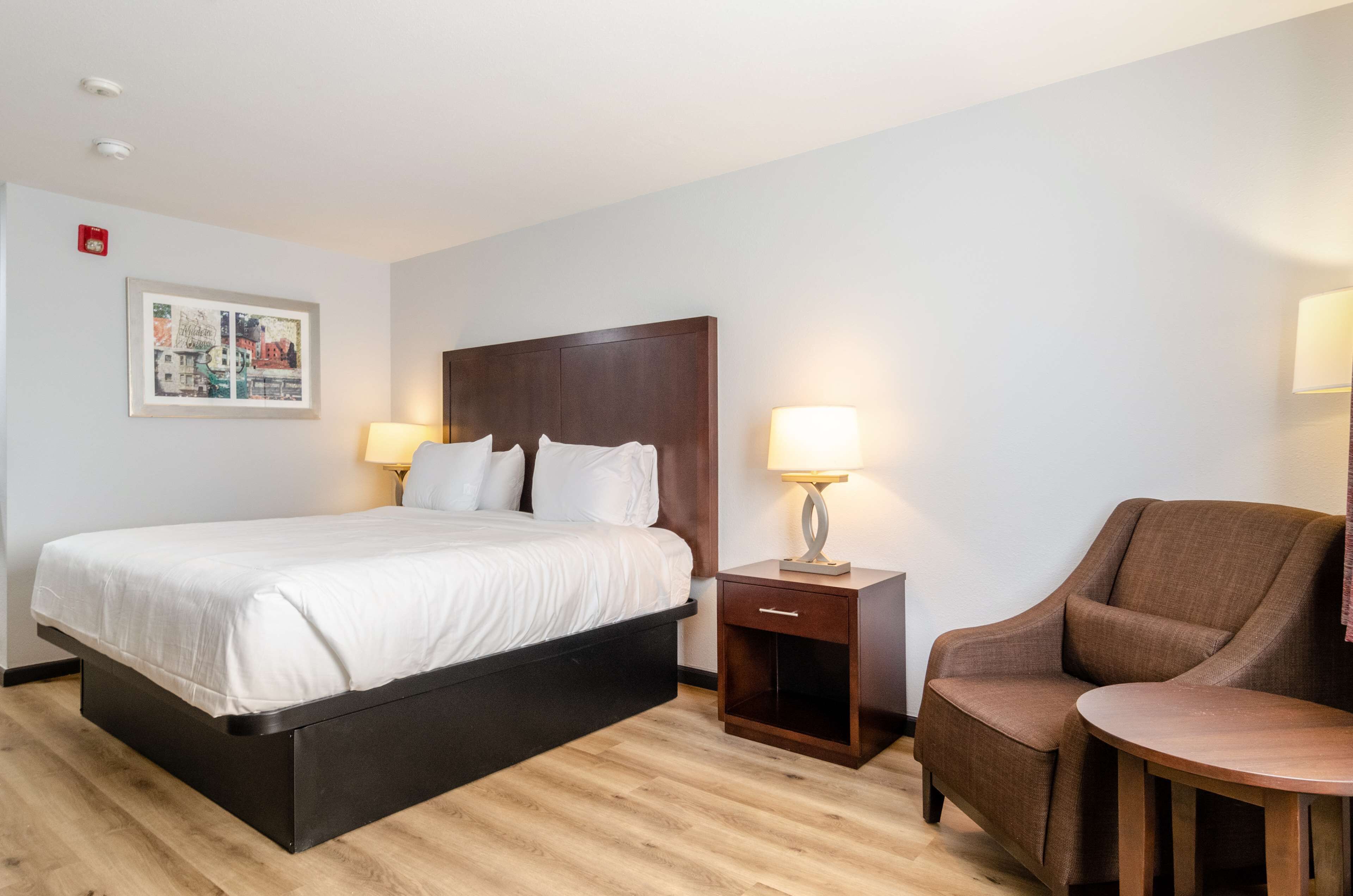 Una habitación de hotel con cama, mesita de noche, silla y una pequeña mesa.