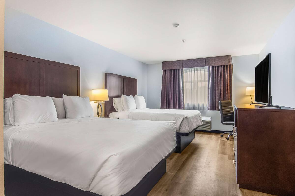 A hotel room with two beds, a desk, a chair, a TV, and a window with curtains.