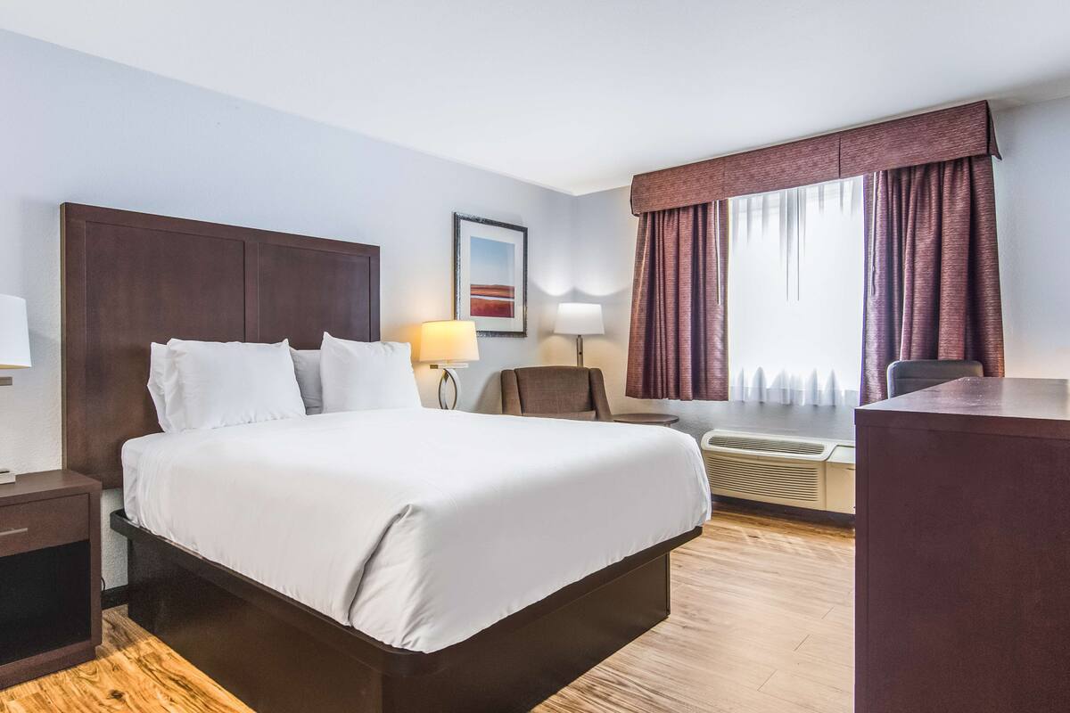 A hotel room with a large bed, a desk, a chair, a lamp, and a picture on the wall.