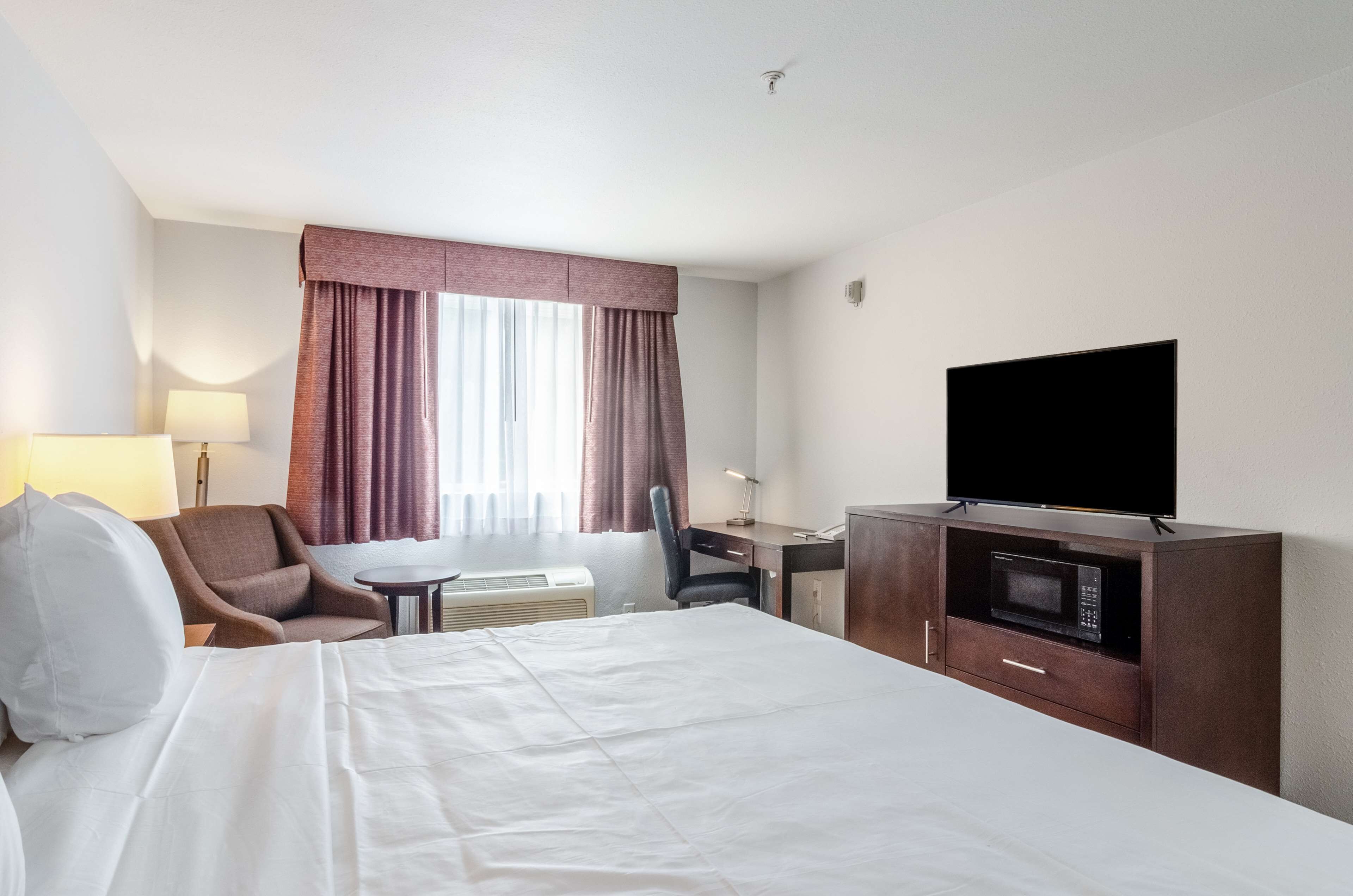 A hotel room with a bed, a desk, a chair, a television, and a microwave.