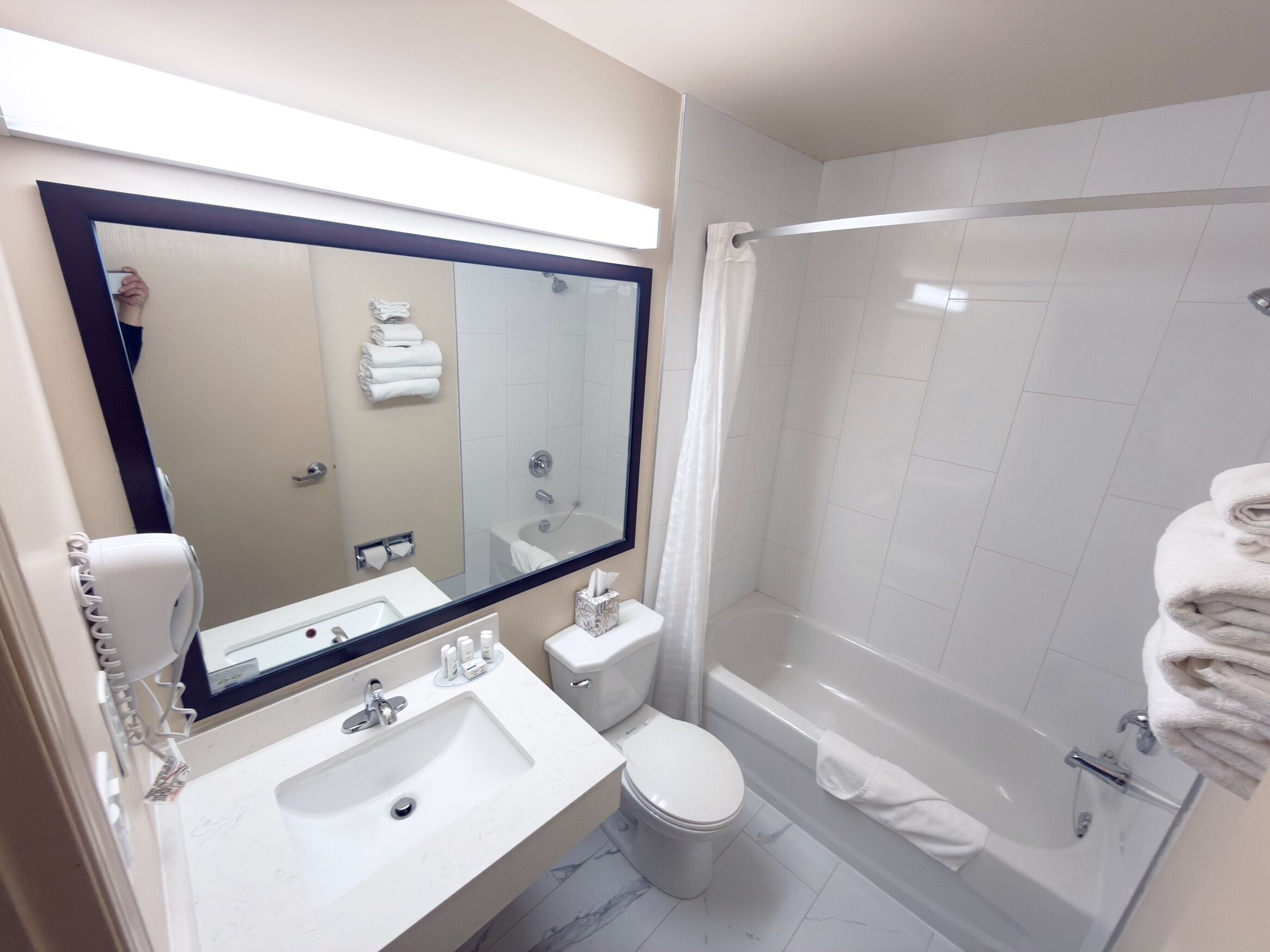 A modern bathroom with a large mirror, sink, toilet, and a walk-in shower.