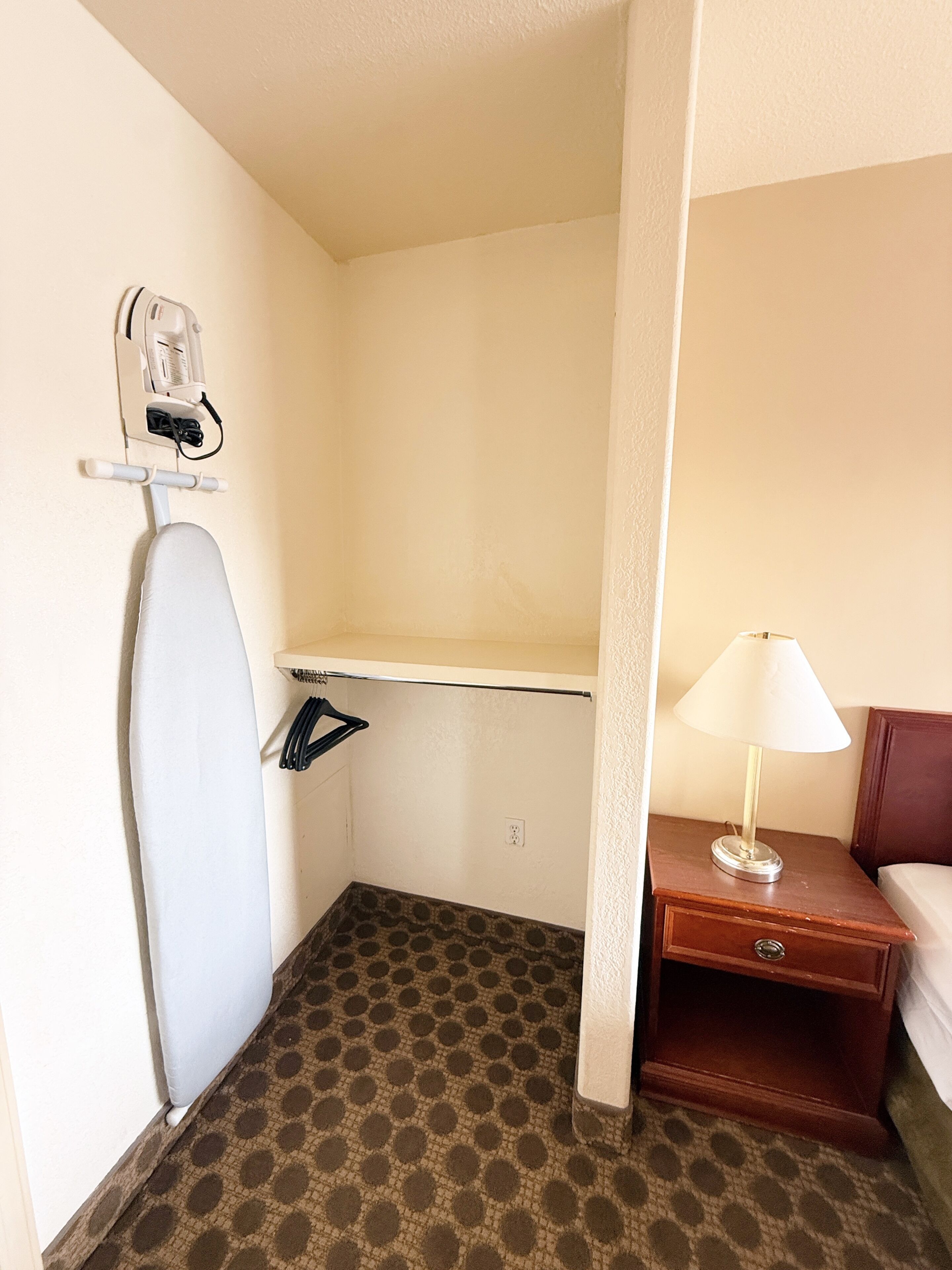 A hotel room with a shower, a small table with a lamp, and a wall-mounted ironing board.