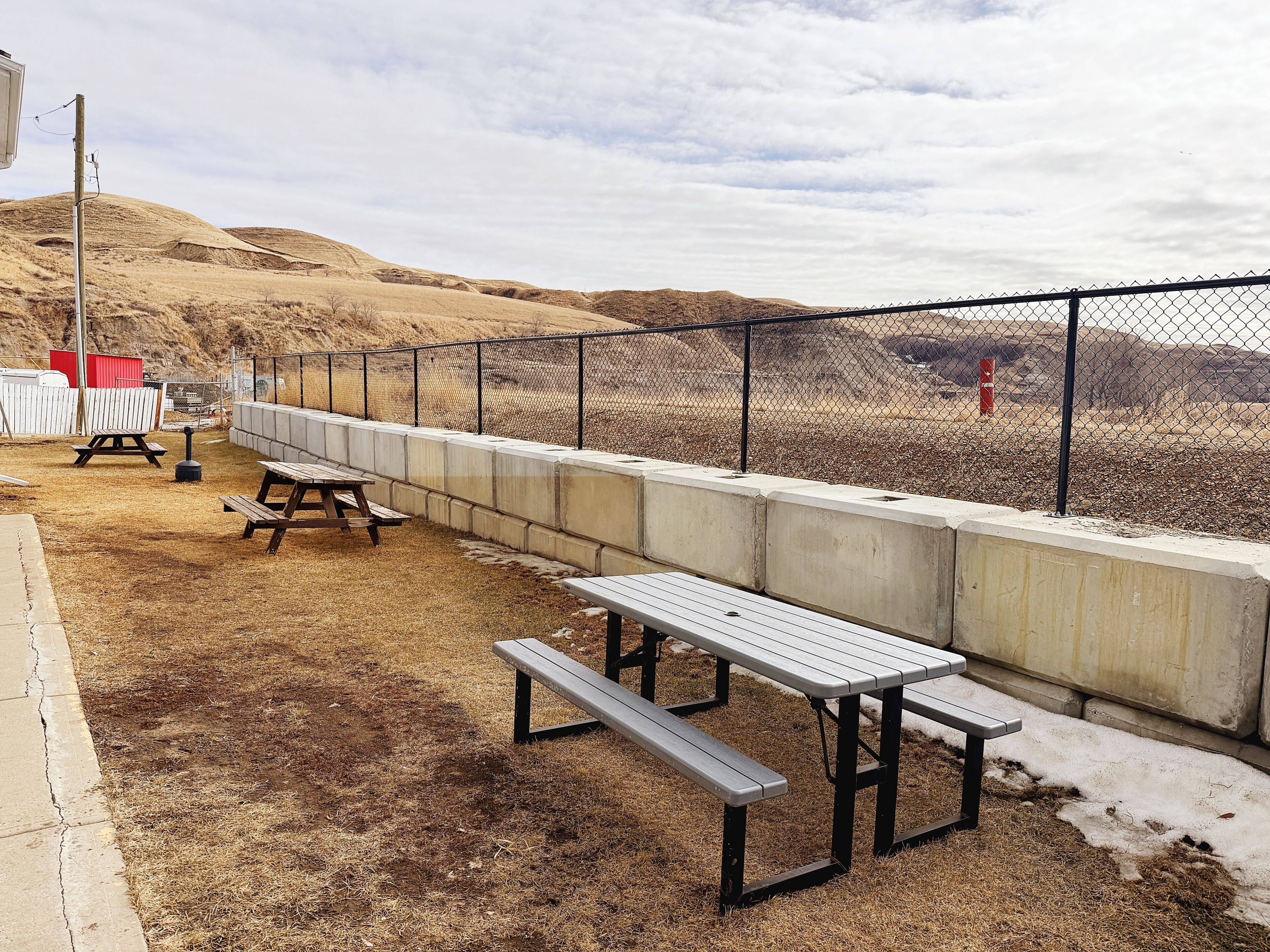 Un espace de pique-nique équipé de bancs et de tables, une clôture en treillis métallique et, au loin, un paysage vallonné.