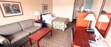 Habitación de hotel con sofá, cama con colcha floral, escritorio de madera y espejo.
