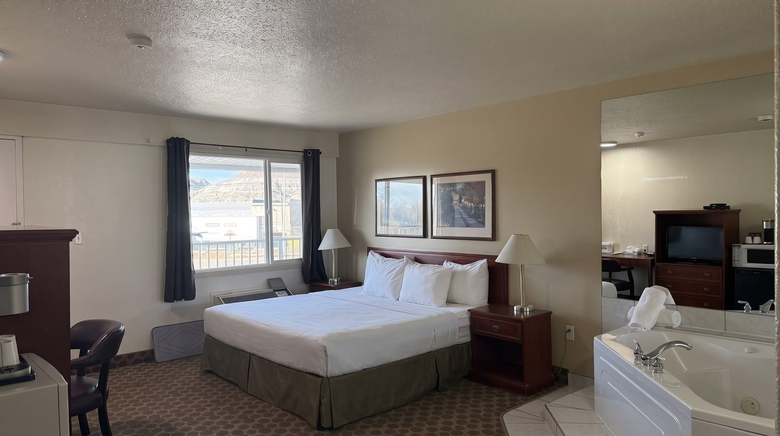 Habitación de hotel con cama, escritorio, silla, lámpara de escritorio, mesita de noche, televisor, microondas y baño con lavamanos y bañera.