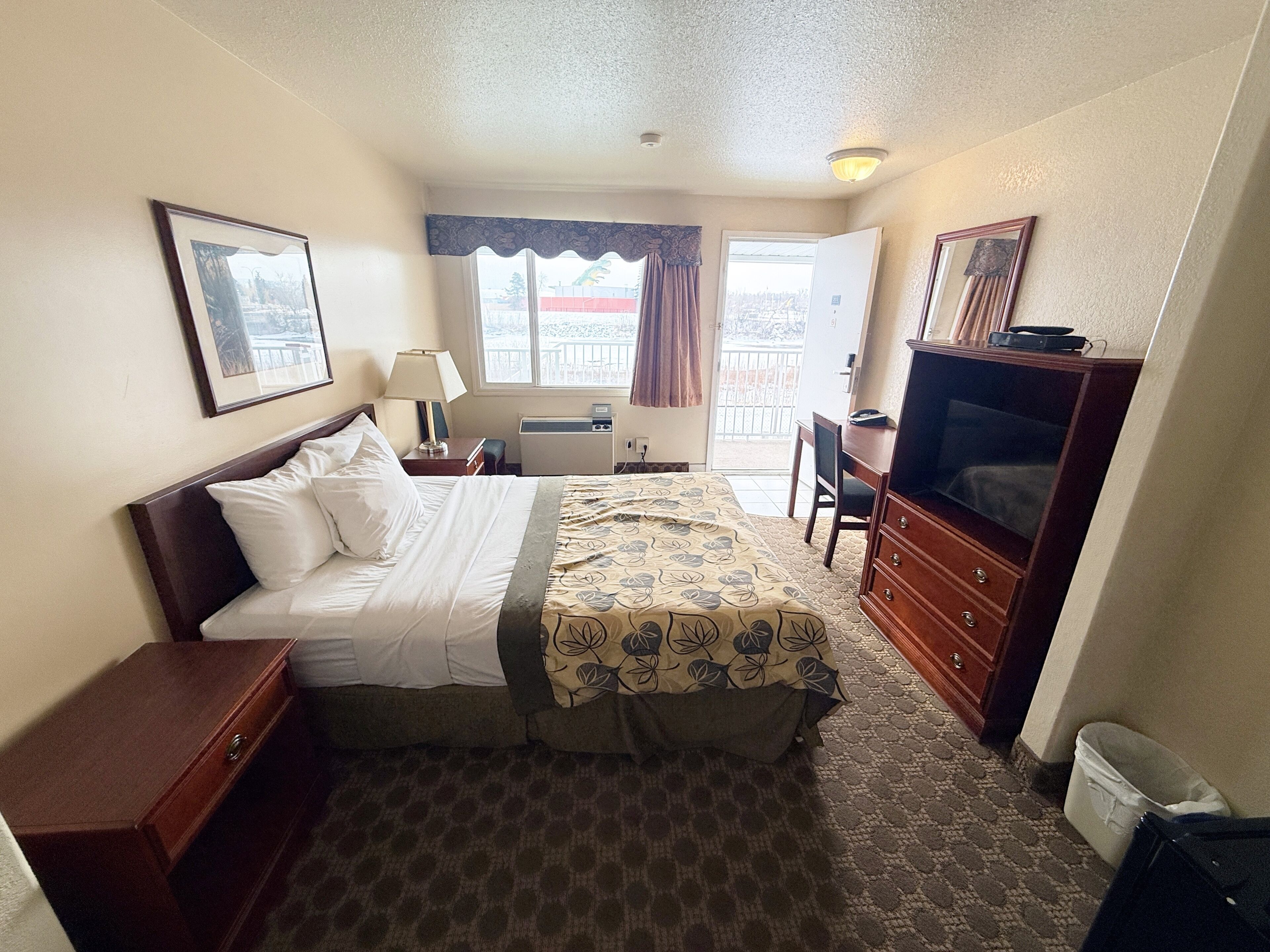 A hotel room with a bed, a desk, a television, a dresser, and a window with curtains.