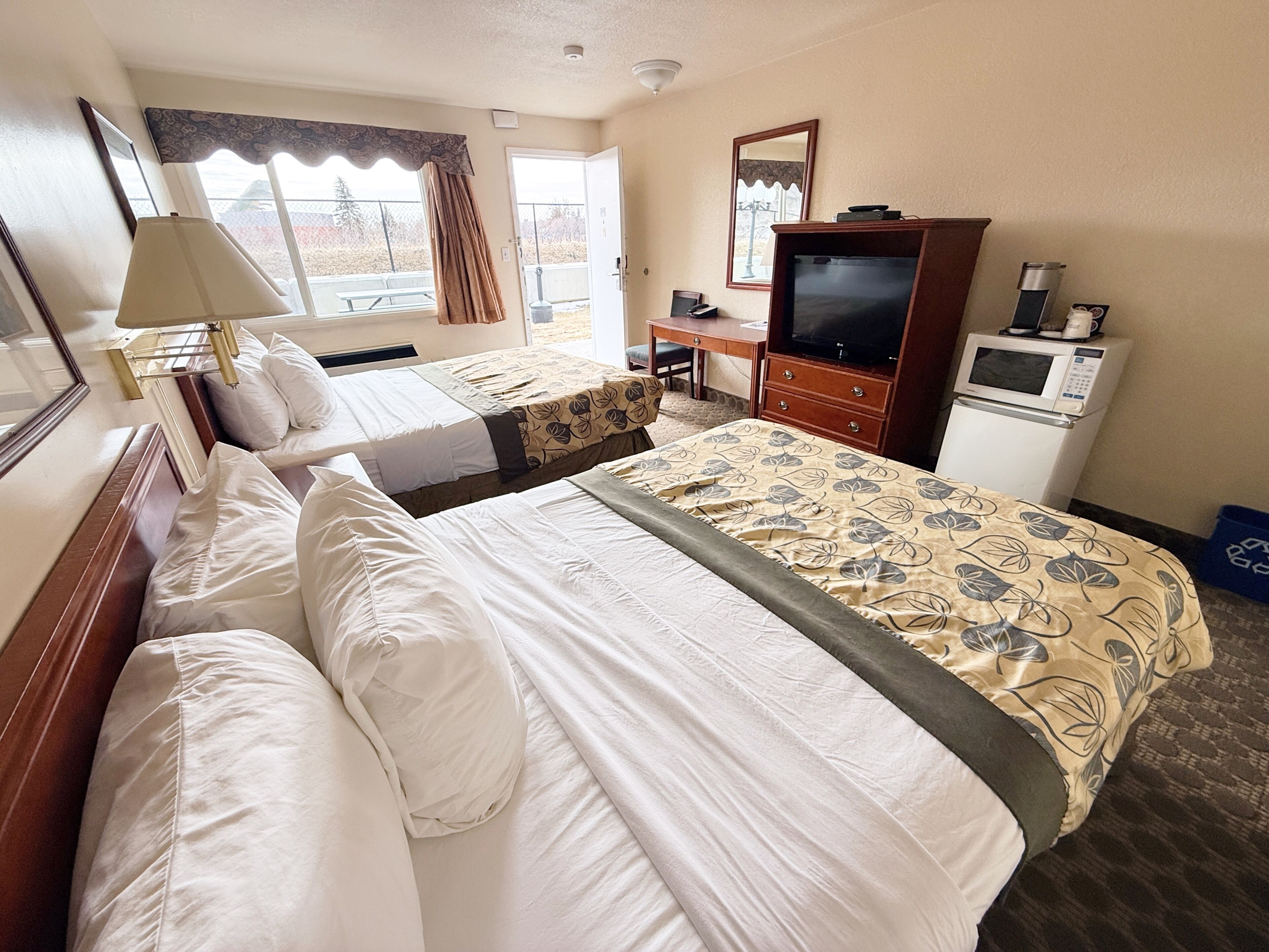 A hotel room with two beds, a desk, a television, a microwave, and a window with curtains.
