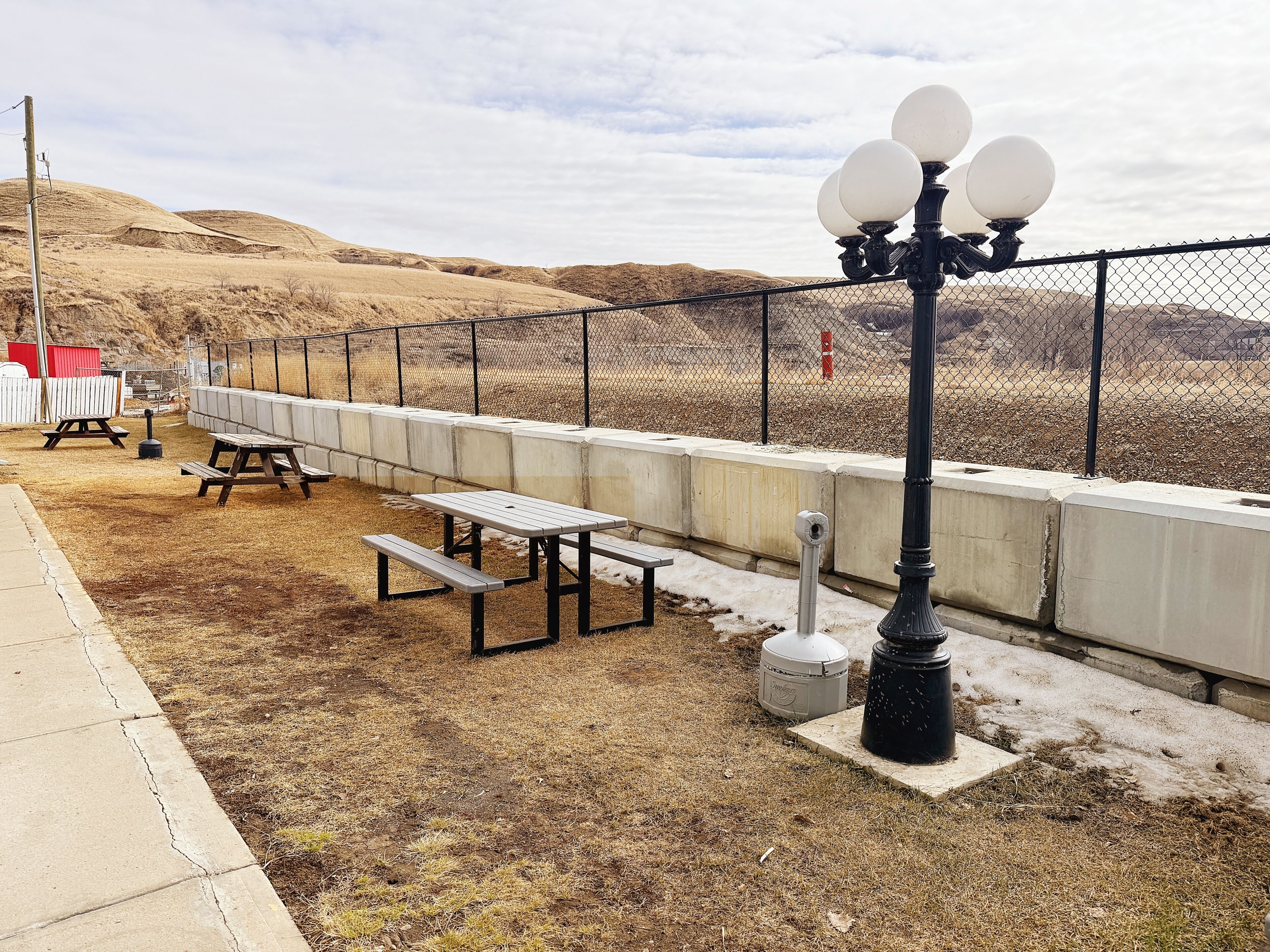 A picnic area with benches and a trash can, a fence, and a lamp post.