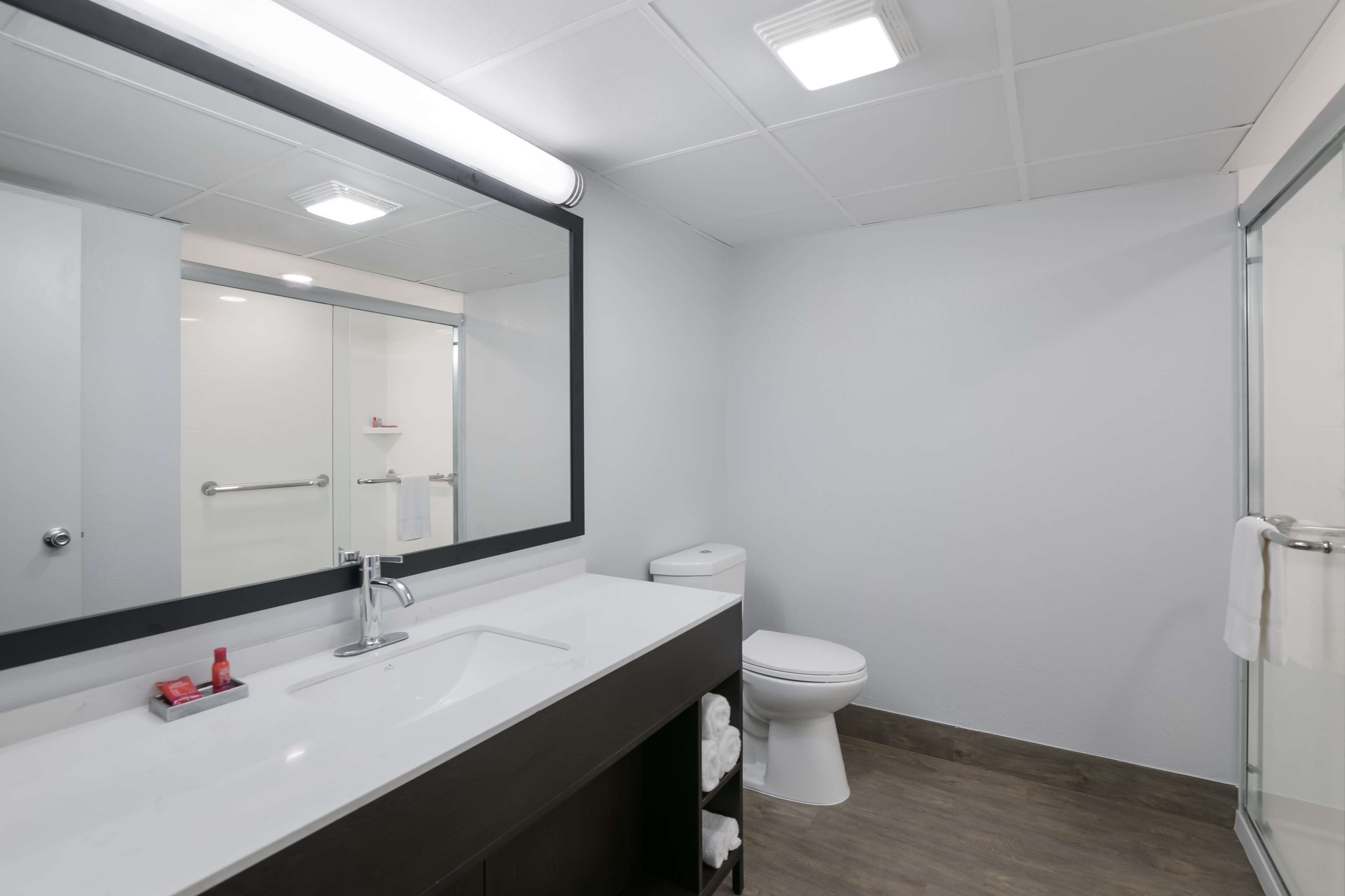 Ein modernes Badezimmer mit großem Spiegel, weißem Waschbecken und Toilette.
