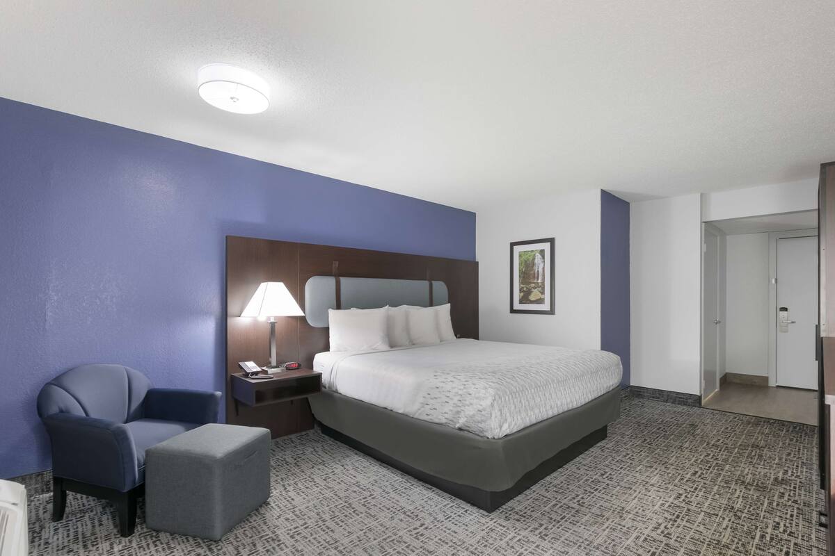 Une chambre d’hôtel avec un lit, une chaise, une table de chevet, une lampe et un tableau au mur.