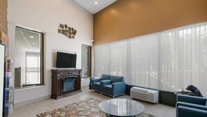 A living room with a fireplace, a television, a blue sofa, a glass coffee table, and a large window with sheer curtains. - SureStay Plus Hotel by Best Western Gatlinburg (Gatlinburg)
