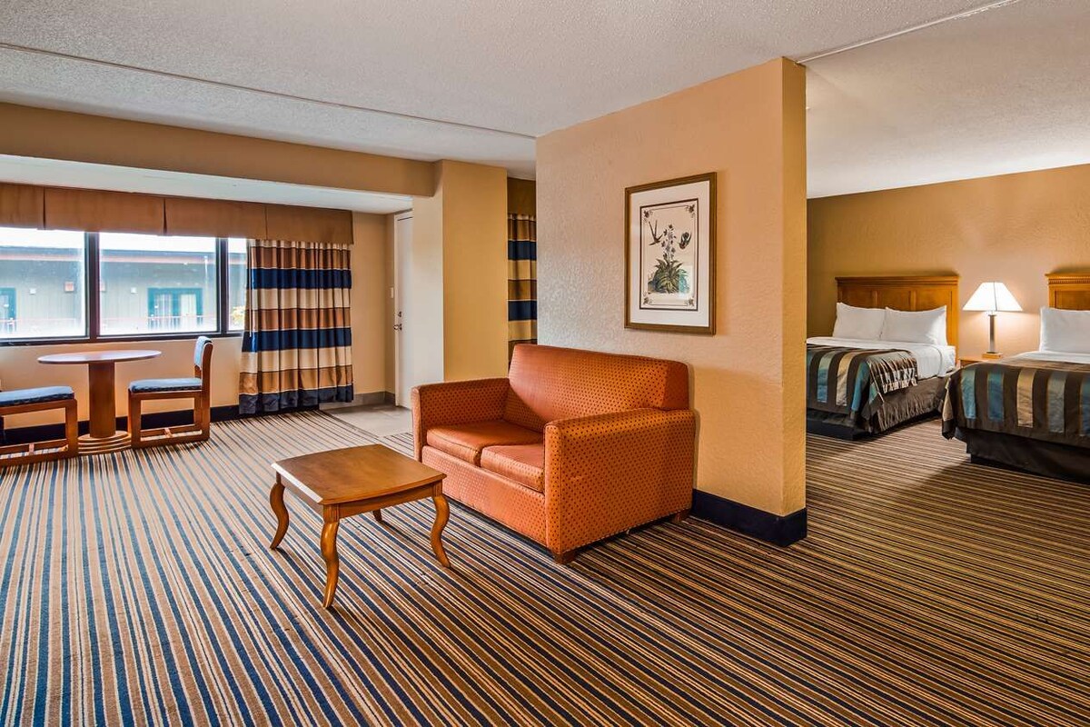 Ein Hotelzimmer mit einem Einzelbett, einer Schlafcouch, einem kleinen Tisch und einem Fenster mit Vorhängen.