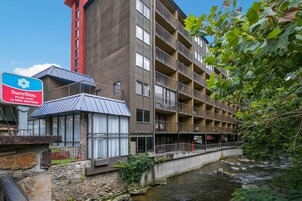 Un hotel de varios pisos con fachada de piedra, un vestíbulo con paredes de vidrio y un río a su lado.