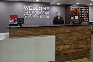 Un mostrador de recepción con un cartel que dice 'WELCOME TO THE KEYSTONE STATE', una insignia de 'Hilton Honors', un quiosco de autoservicio y una barra de aperitivos.