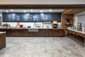 A modern breakfast area with a chalkboard menu, a coffee machine, and a variety of food items.