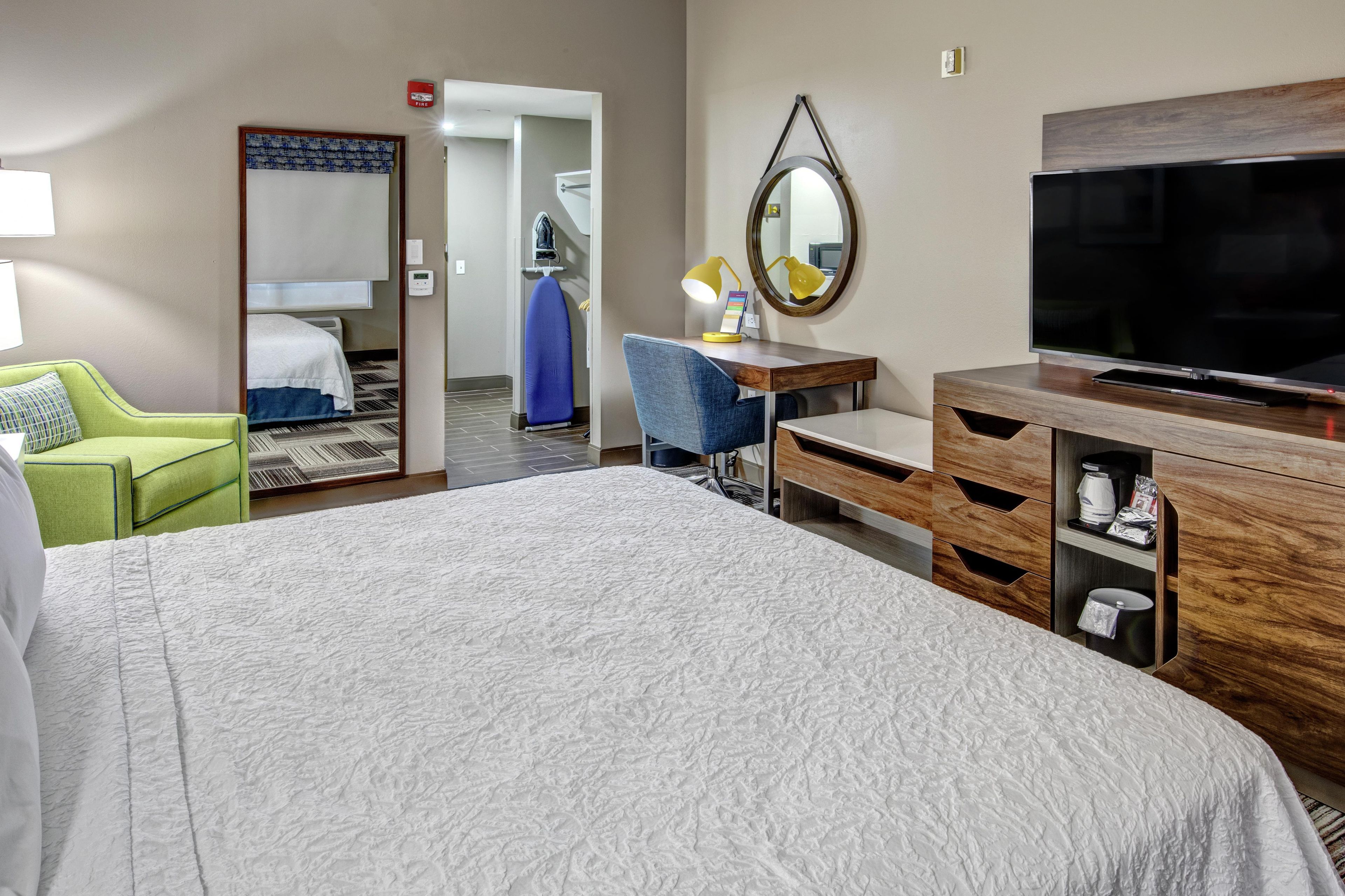 A hotel room with a bed, a desk with a chair, a television, and a mirror.