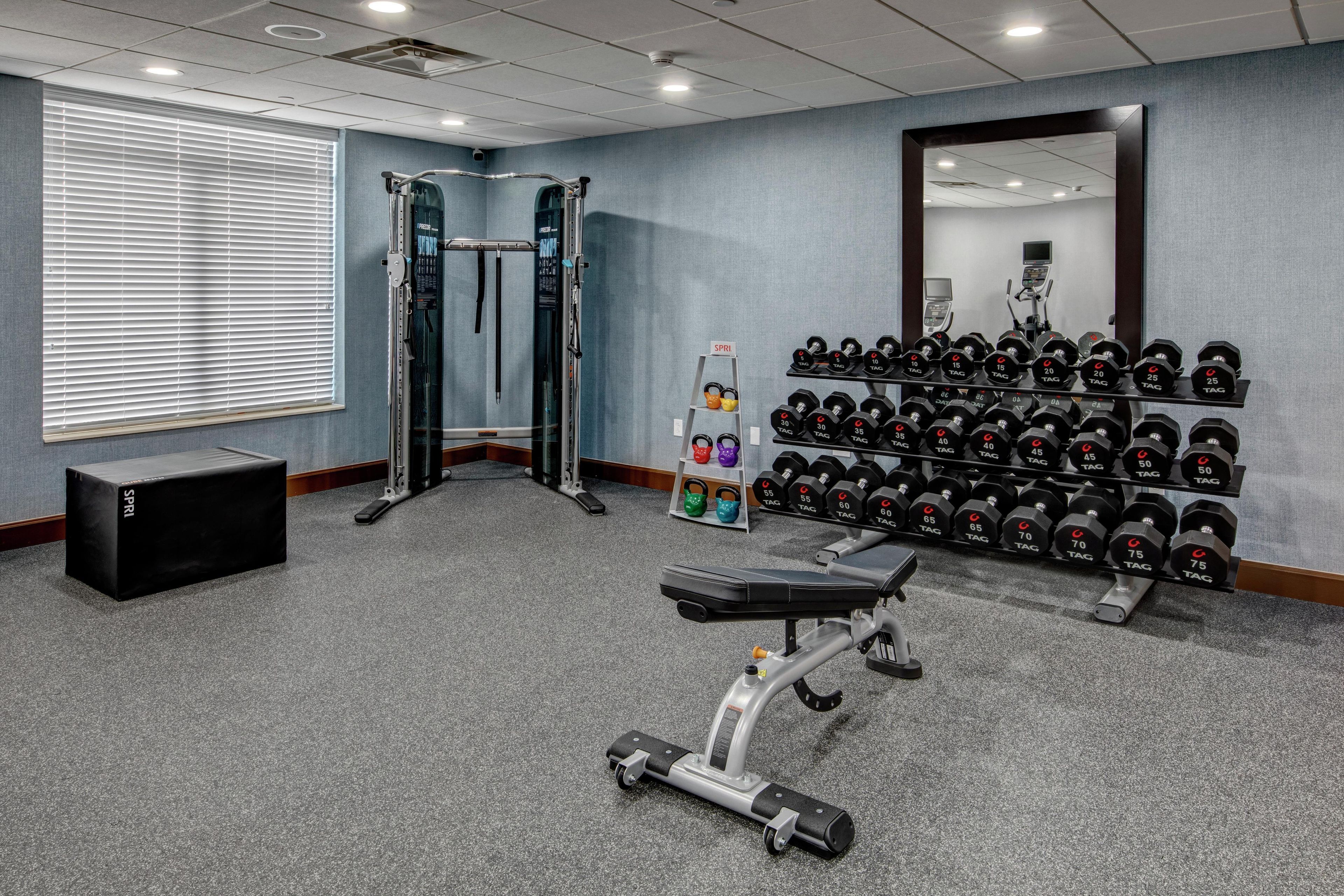 A gym with weightlifting equipment, a bench, and a mirror on the wall.