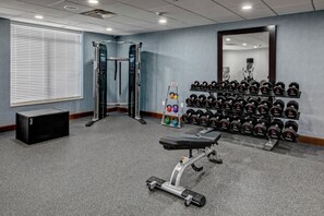 Un gimnasio con equipo de levantamiento de pesas, una banca y un espejo en la pared.