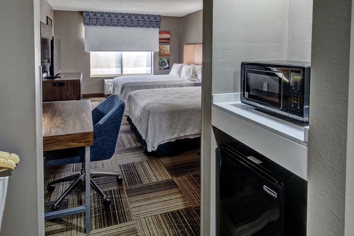 A hotel room with two beds, a desk, a chair, a microwave, and a mini-fridge.