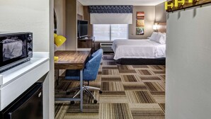 A hotel room with a bed, a desk with a chair, a television, a microwave, and a patterned carpet.