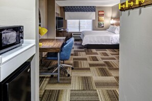 Habitación de hotel con cama, escritorio, silla, televisor y microondas.