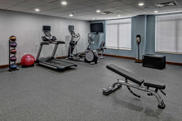 A gym with treadmills, elliptical machines, a bench, and a set of exercise balls.