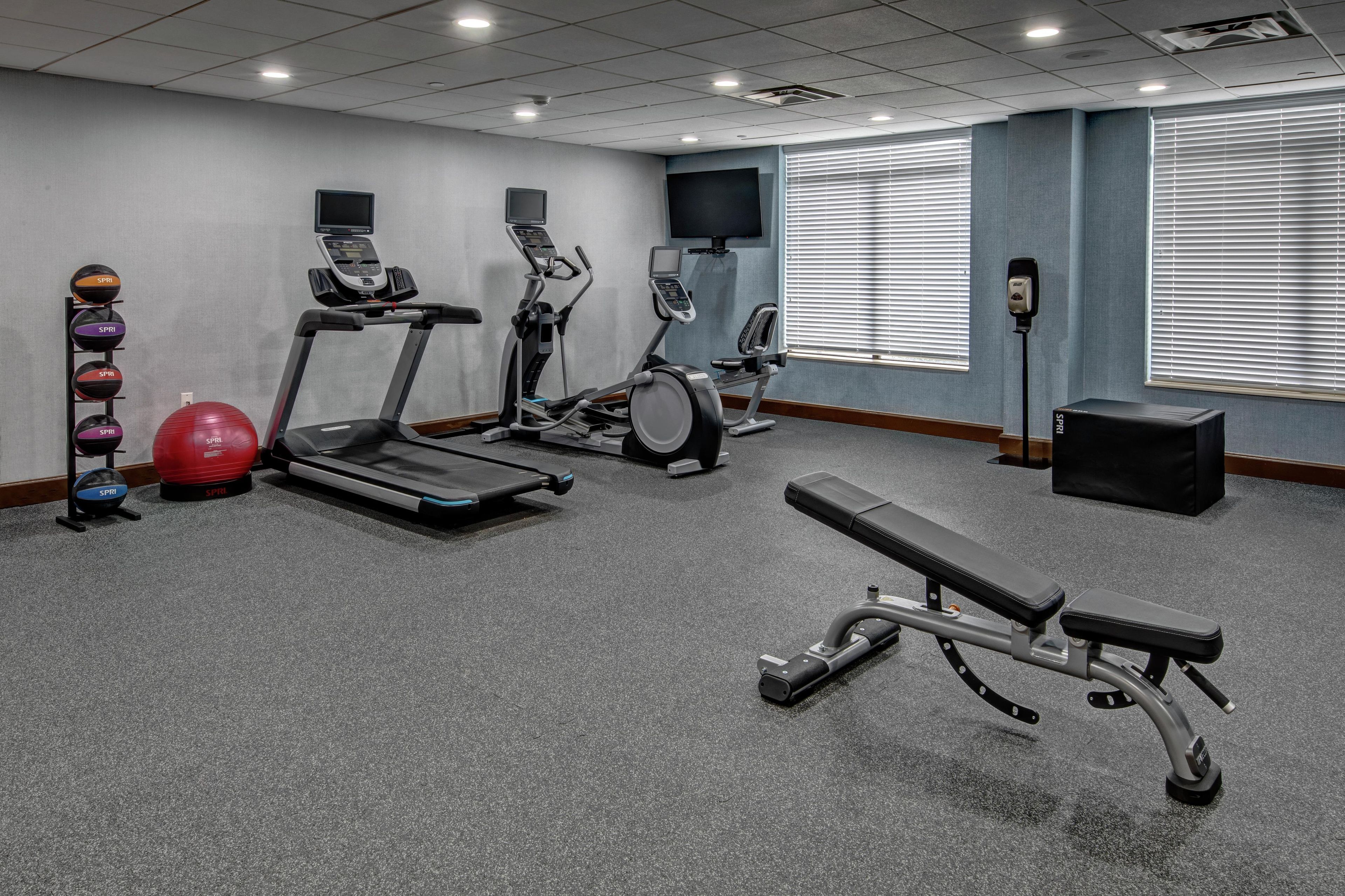 Een fitnessruimte met loopbanden, crosstrainers, een bankdrukpers en diverse fitnessballen.