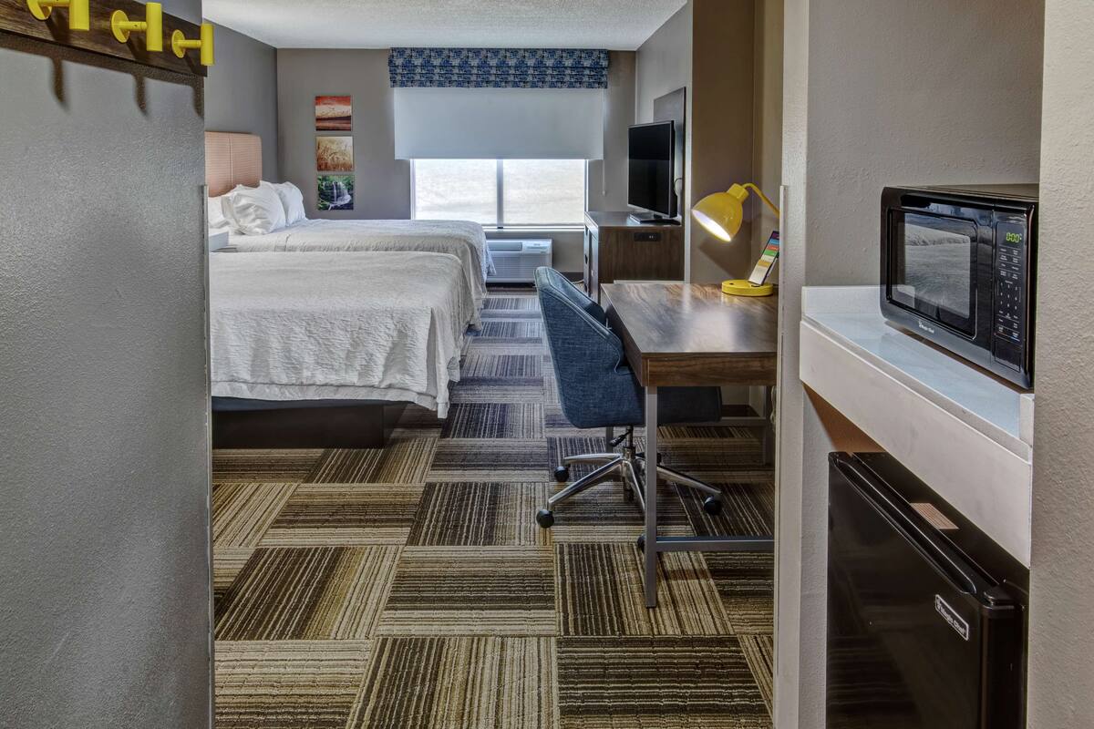 A hotel room with two beds, a desk with a chair, a television, a microwave, and a refrigerator.