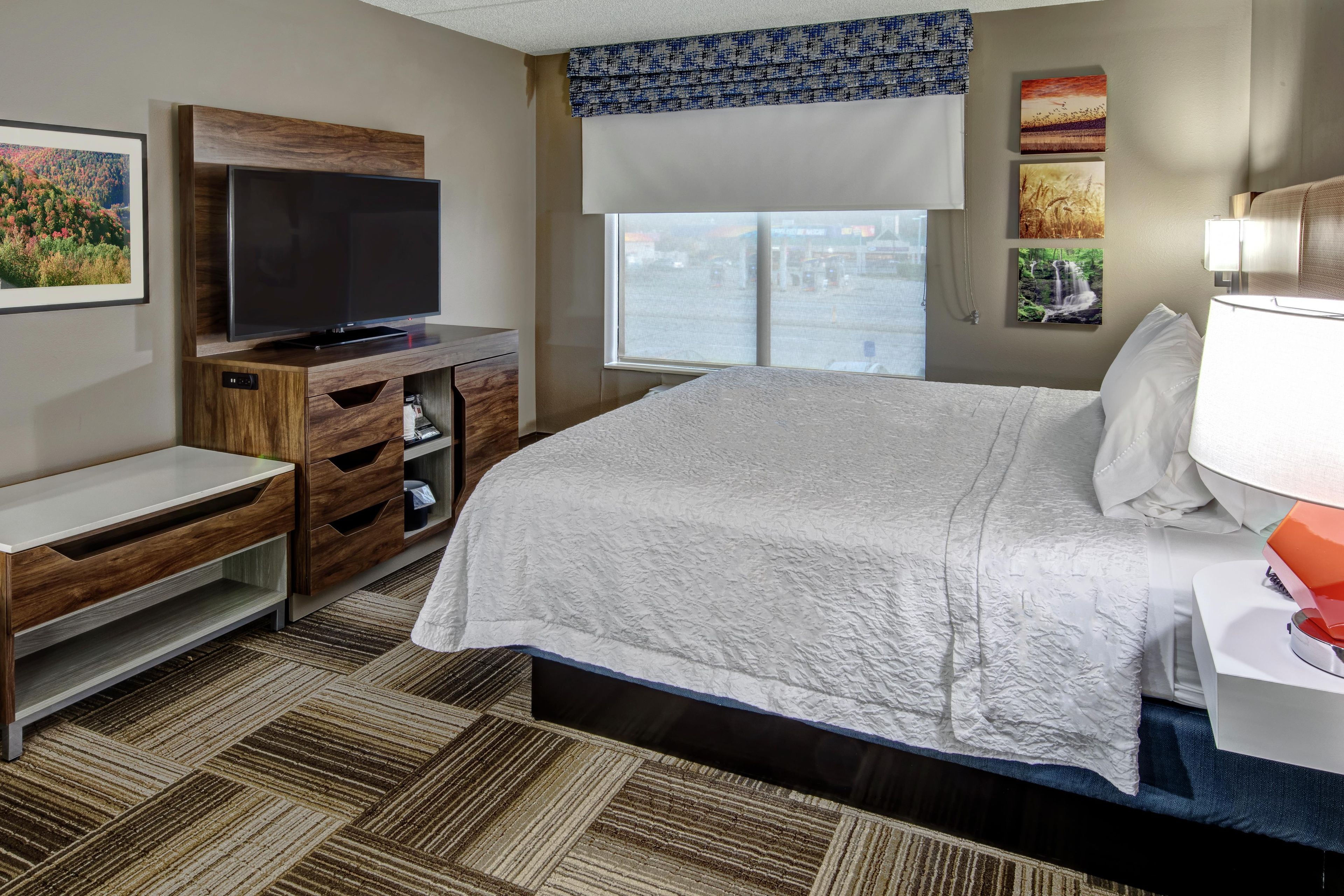 A hotel room with a bed, a television, a desk, and a window with a view of the city.